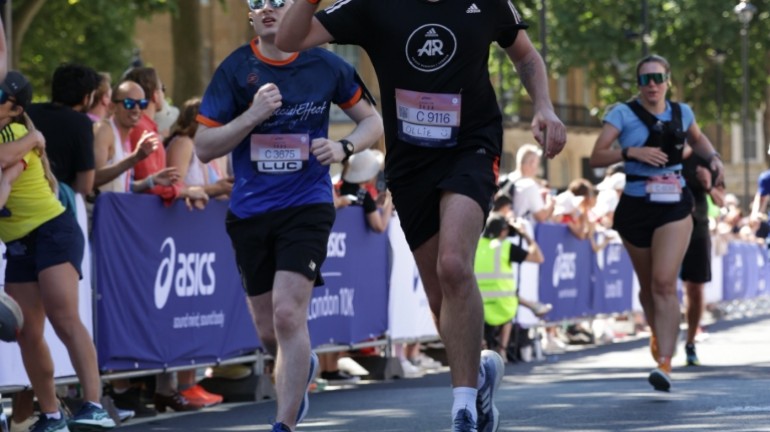 A picture of myself (Luc Shelton) running the final stretch of the ASICS London 10K. I am running alongside someone who is waving.